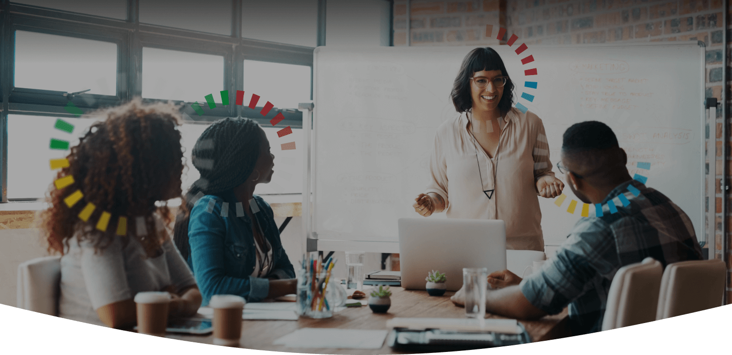 Woman standing in front of her team leading a meeting in a colorful working space. All people have DiSC style halos. 