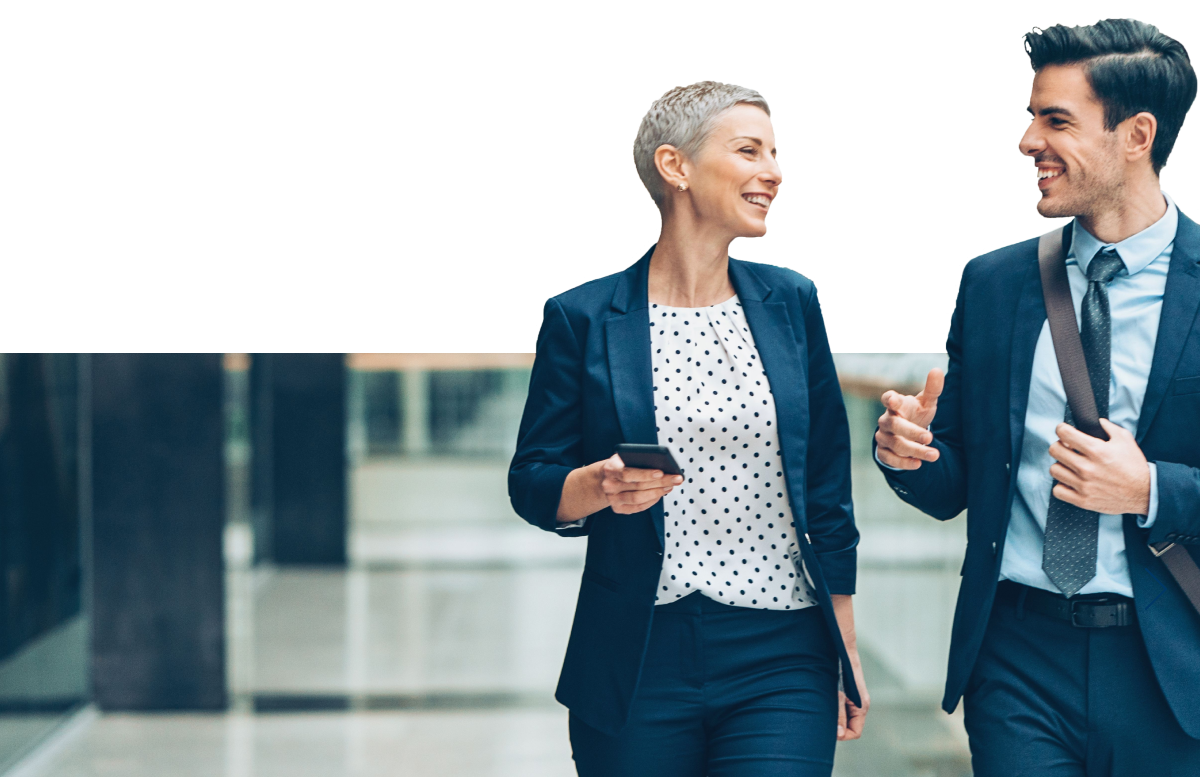 Two smiling coworkers walking together down an office hallway.