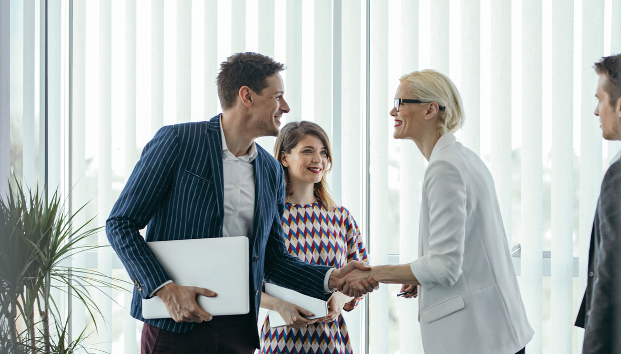 Two men shaking hands wearing semi casual business attire while in an office setting.